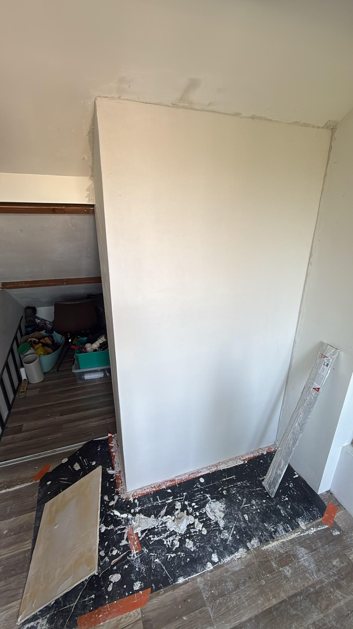 Nieuw geplaatste en sausklaar gestucte wand naast een trapgat onder een schuin dak in Breda